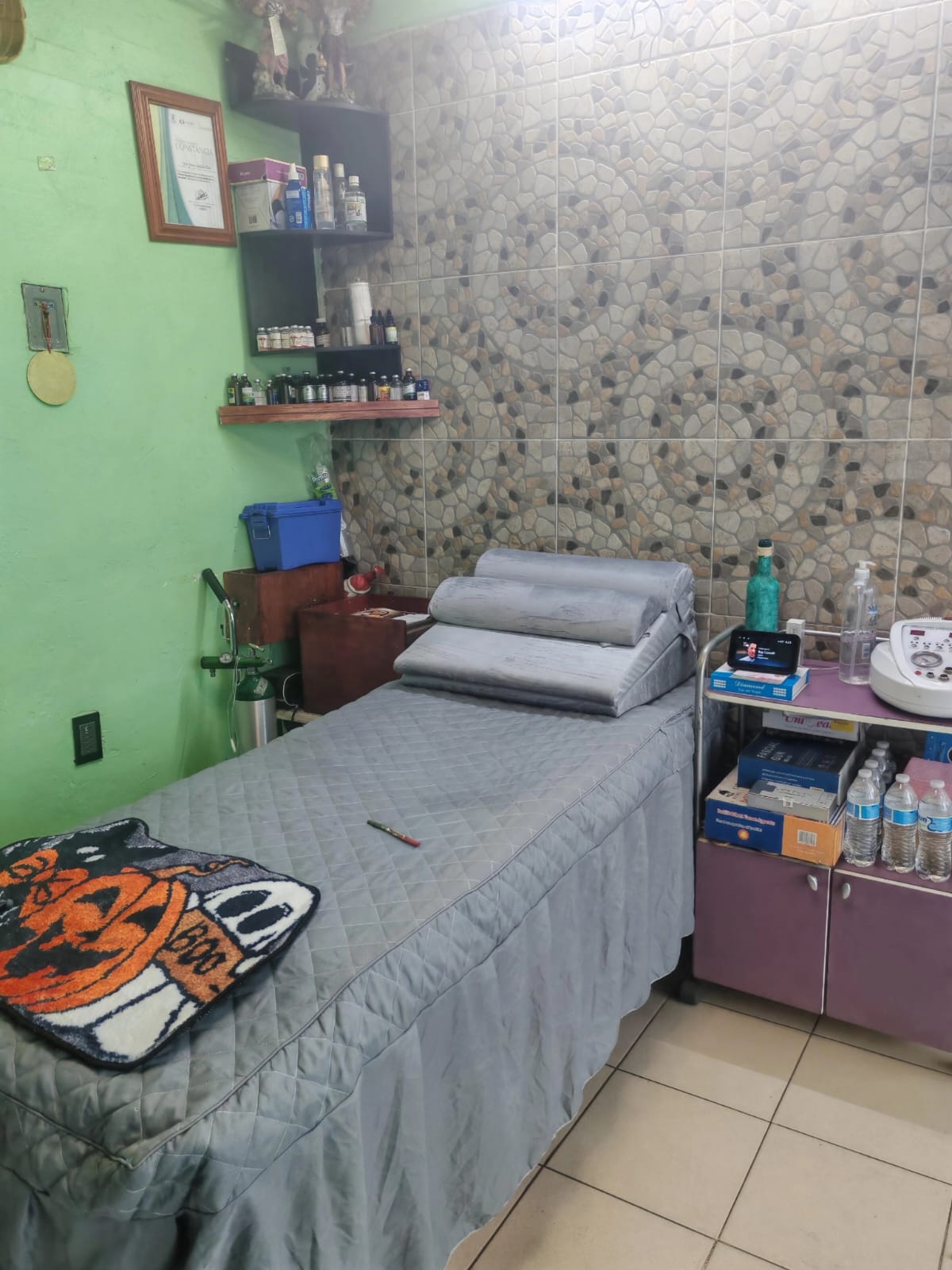 Cabina de terapias alternativas del consultorio de Mercado Concordia, con camilla gris y repisas de madera con esencias